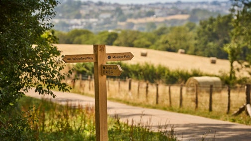Image of new wayfinding post in front of field with hay bales showing Saltram's new walks on the east side of the estate